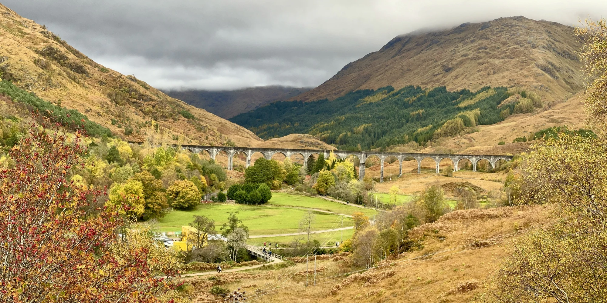Le viaduc de Glenfinnan entre les collines et les arbres d’automne, sous les nuages.